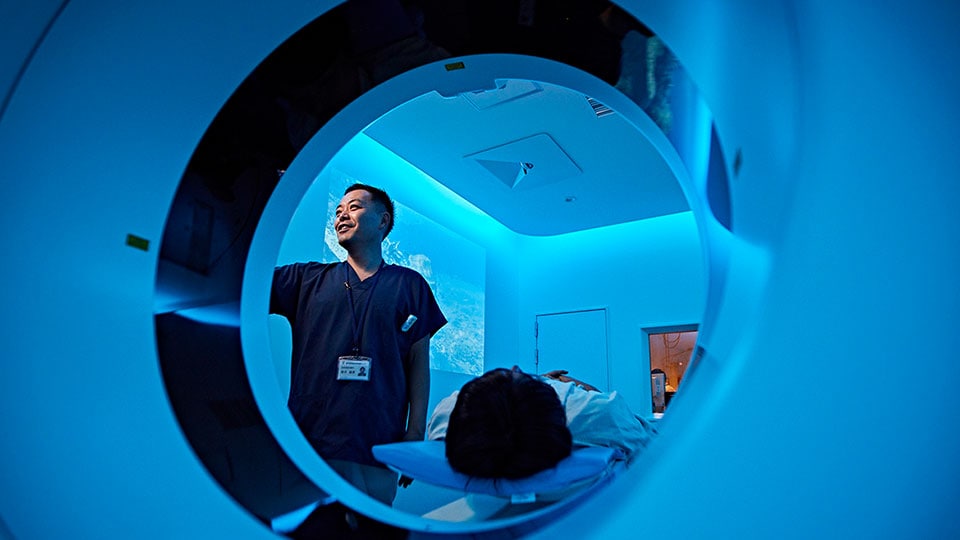 Foto eines Klinikers, der einen Scan am Portal des CT-Scanners vorbereitet, wobei sich der Patient auf dem Patiententisch des CT-Systems befindet