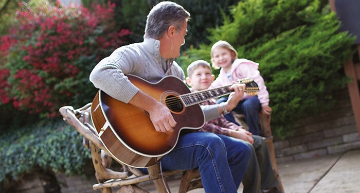 Auf einer Bank sitzender Mann, der Gitarre spielt und dabei seine Sauerstoffbehandlung erhält