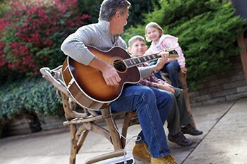 Auf einer Bank sitzender Mann, der Gitarre spielt und dabei seine Sauerstoffbehandlung erhält