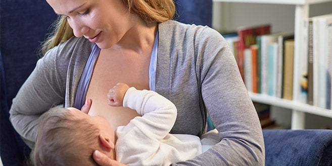Eine Mutter zeigt den Kreuzwiegengriff, bei dem sie ihr Baby mit einem Arm stützt und mit dem anderen ihre Brust hält.