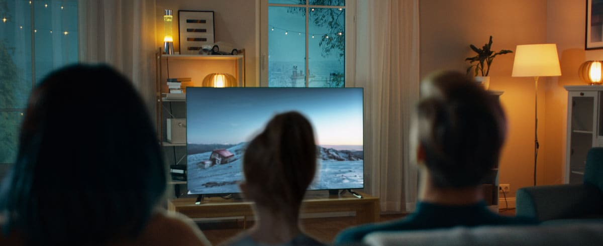Eine Familie sitzt zusammen im Wohnzimmer und schaut gemeinsam auf einem großen Fernseher fern