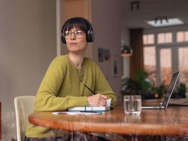Eine Person, die bequeme Philips Kopfhörer trägt, sitzt an einem Tisch mit einem Notizbuch und einem Laptop