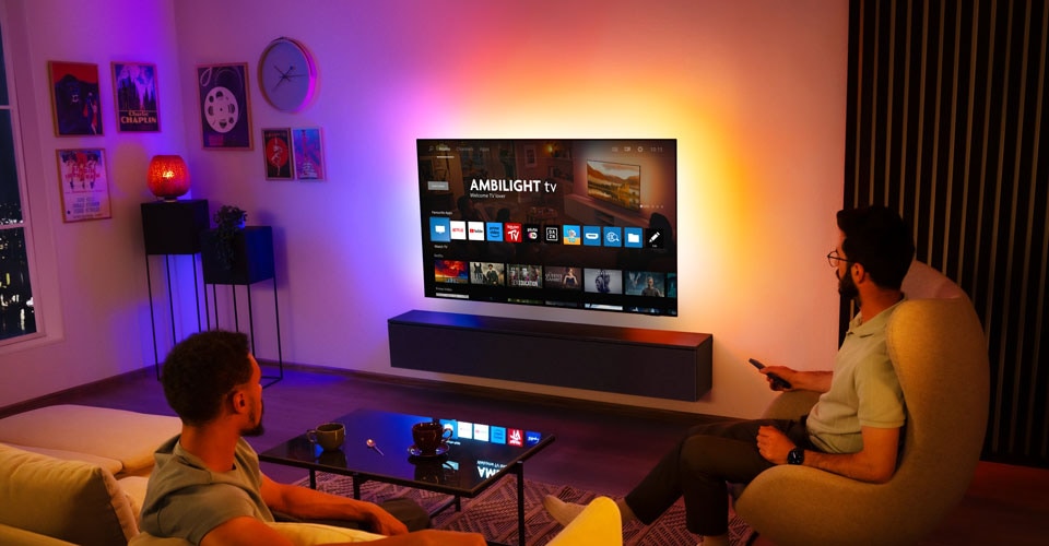 Zwei Männer schauen in einem Wohnzimmer auf einem an der Wand montierten Ambilight-Fernseher