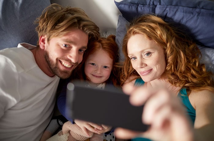 Junge Eltern lächeln mit ihrer Tochter in eine Kamera, um ein Selfie zu machen,