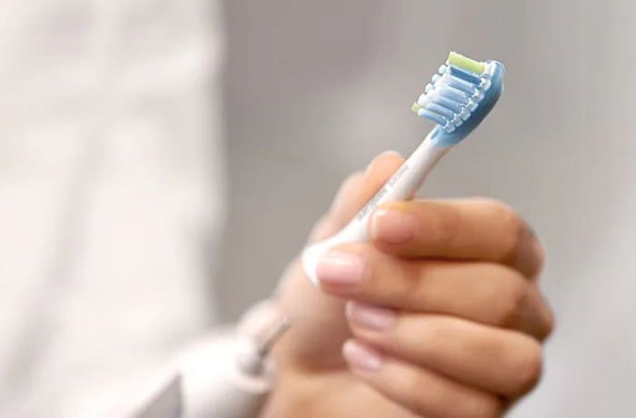 Eine Person steckt einen abnehmbaren Bürstenkopf auf eine weiße elektrische Zahnbürste.