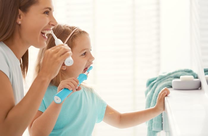 Ein junges Mädchen und ihre Mutter putzen ihre weißen Zähne mit elektrischen Zahnbürsten.