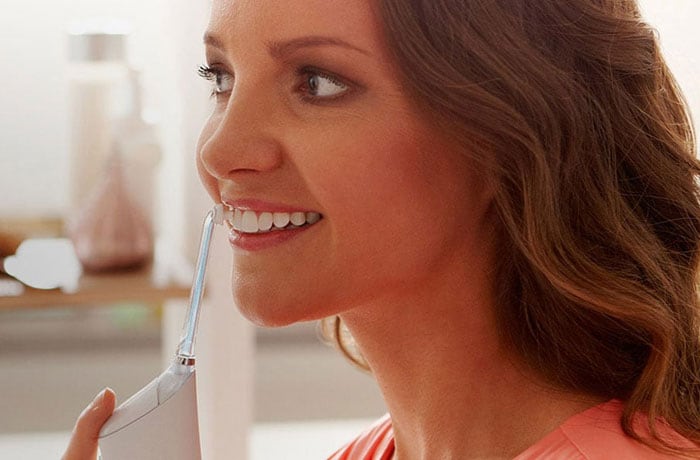 Eine Frau schaut gerade aus und putzt ihre weißen Zähne mit einem Philips Sonicare Airfloss.