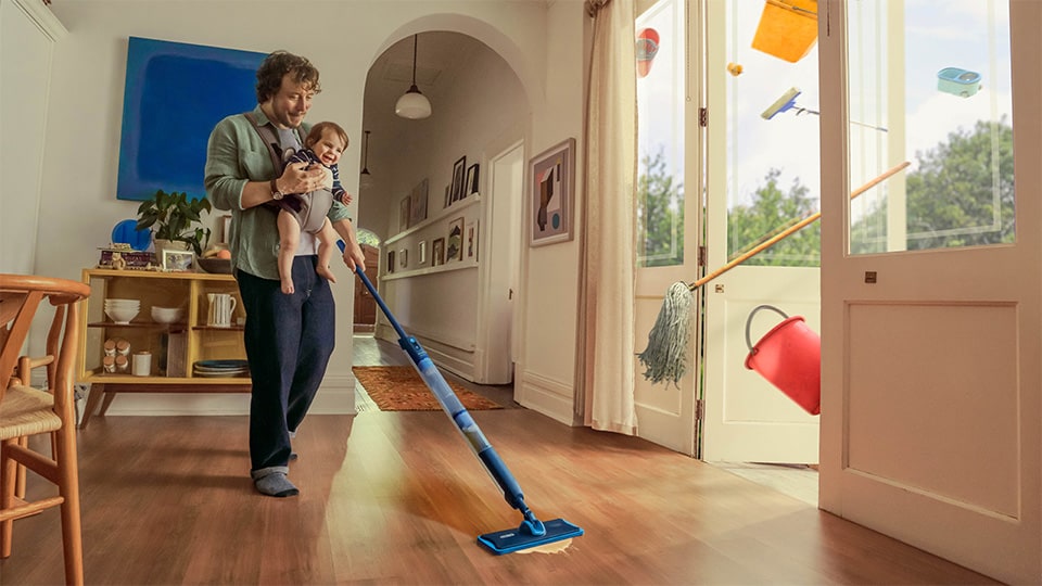 Ein Mann trägt sein Baby und reinigt den Boden mit dem Philips OneUp elektrischen Wischmopp