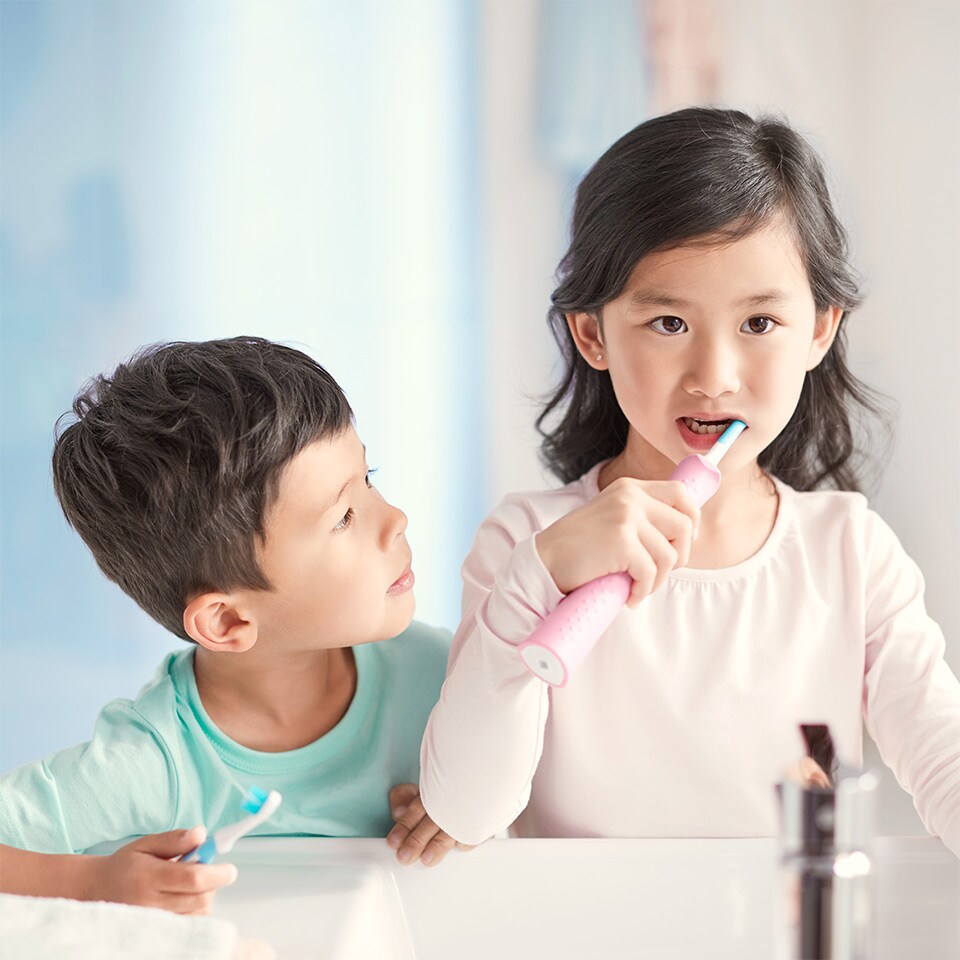 Mädchen zeigt ihr Lächeln und hält eine Sonicare For Kids Schallzahnbürste in der Hand