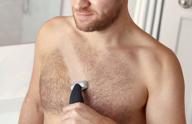 Oberkörper eines Mannes, der mit einem Rasierer eine Linie in sein Brusthaar rasiert.