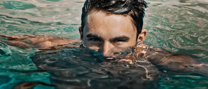 Ein Mann mit dunklen Haaren blickt mit seinem Gesicht halb im Wasser in die Kamera auf.