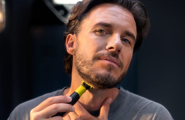 Nahaufnahme eines Mannes, der vor einem Spiegel die Bartkante seines dunklen Bartes mit dem Philips OneBlade trimmt