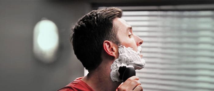 Seitliches Profil eines Mannes, der sich mit einem elektrischen Rasierer rasiert.